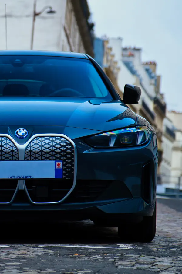 Gros plan sur l'avant d'une BMW Série 4 noire, mettant en valeur sa large calandre distinctive à motif en nid d'abeilles et ses phares LED agressifs, photographiée sur les pavés parisiens