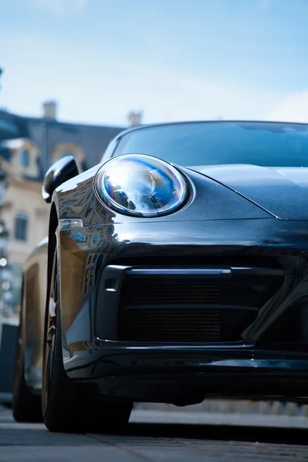 Gros plan sur l'avant d'une Porsche 911 noire, mettant en évidence son phare rond LED caractéristique et sa prise d'air inférieure.