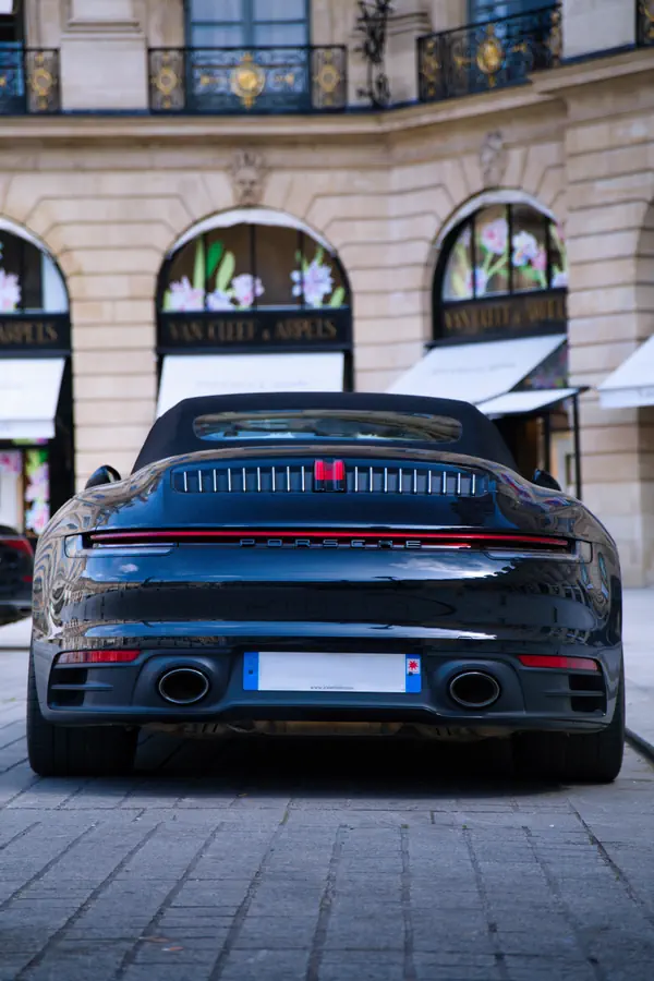 Arrière d'une Porsche 911 noire récente stationnée sur la Place Vendôme, montrant sa bande lumineuse LED rouge caractéristique avec l'inscription "PORSCHE" et ses doubles sorties d'échappement.