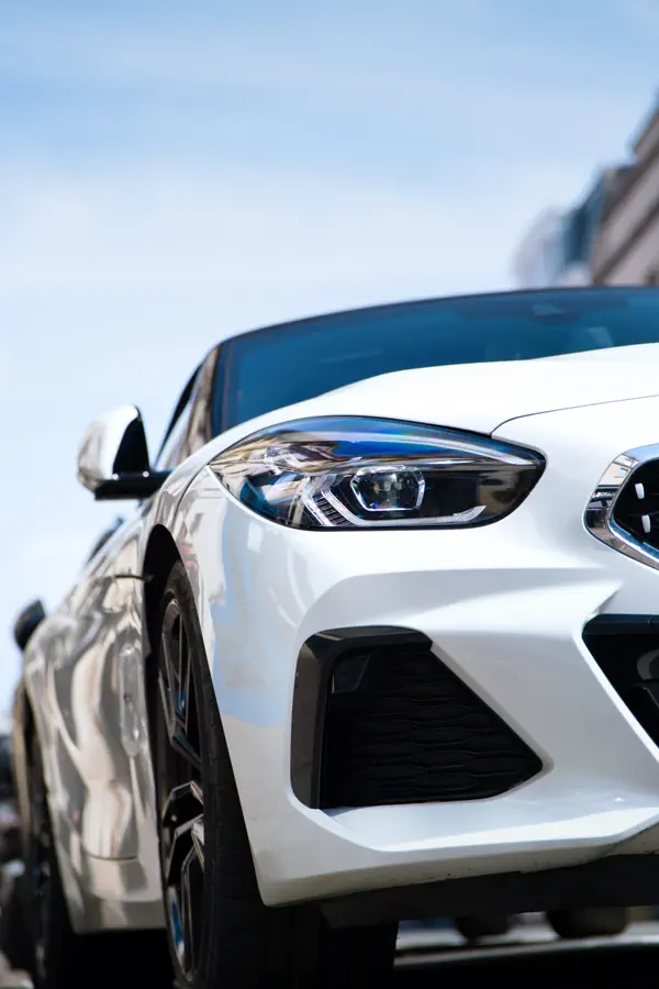 Gros plan sur l'avant d'une BMW Z4 blanche, montrant son phare LED profilé avec signature lumineuse caractéristique et sa large prise d'air inférieure noire.