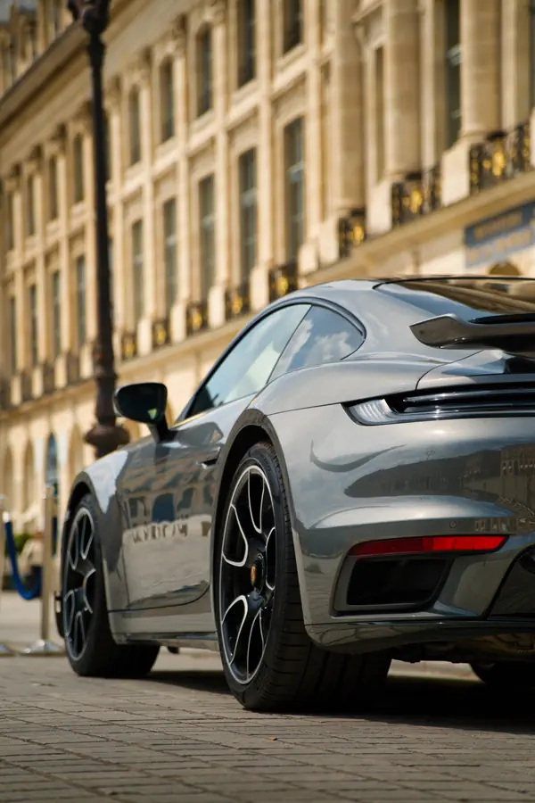Vue de trois-quarts arrière d'une Porsche 911 Turbo gris métallisé stationnée sur les pavés de la Place Vendôme.