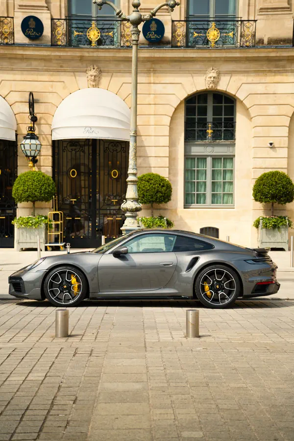 Porsche 911 Turbo gris métallisé photographiée de profil sur la Place Vendôme, devant l'entrée du Ritz Paris.