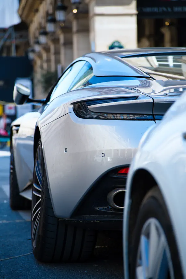Vue de trois-quarts arrière d'une Aston Martin DB11 blanche stationnée dans une rue parisienne.