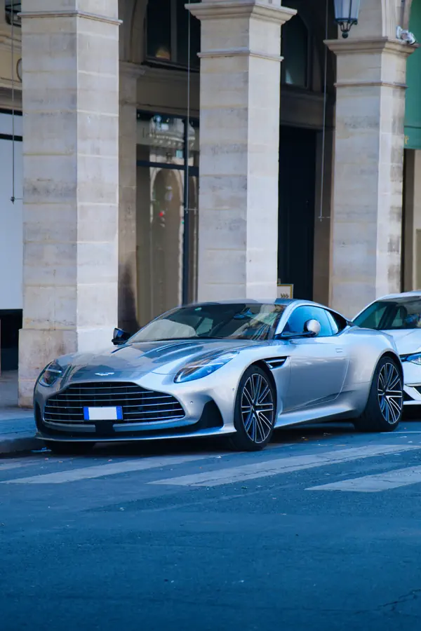Aston Martin DB11 gris argenté stationnée devant un bâtiment parisien aux colonnes de pierre imposantes.