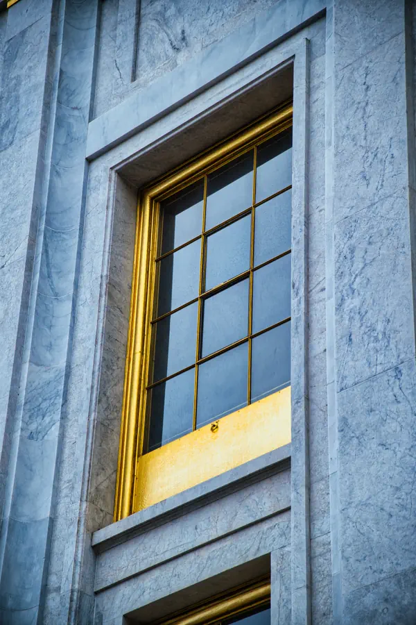 Fenêtre à croisillons encadrée de marbre blanc veiné, avec des détails architecturaux dorés, créant un contraste élégant entre la pierre froide et les éléments métalliques chaleureux