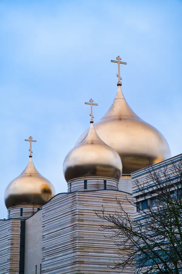 Trois dômes dorés de la cathédrale orthodoxe russe de Paris, surmontés de croix orthodoxes, avec leur architecture contemporaine en pierre claire striée