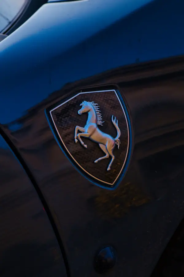 Gros plan sur l'emblème Ferrari, montrant le célèbre cheval cabré argenté sur fond noir dans son écusson, photographié sur la carrosserie noire brillante d'une Ferrari