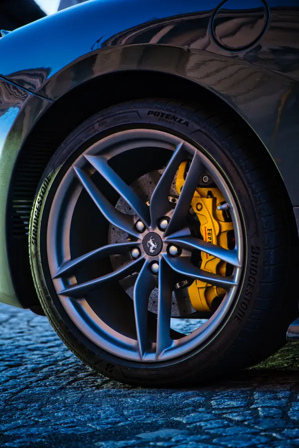 Détail de la roue d'une Ferrari montrant sa jante en alliage gris à cinq branches, son étrier de frein jaune caractéristique et son pneu Bridgestone Potenza, photographiée sur des pavés parisiens