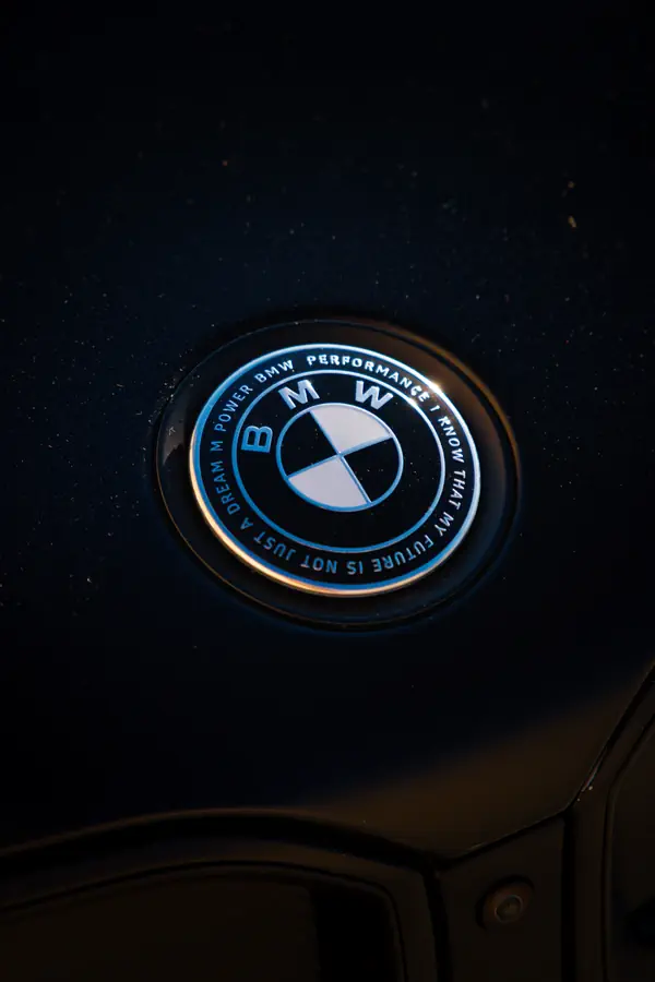 Gros plan sur un badge BMW noir et bleu apposé sur une carrosserie sombre.