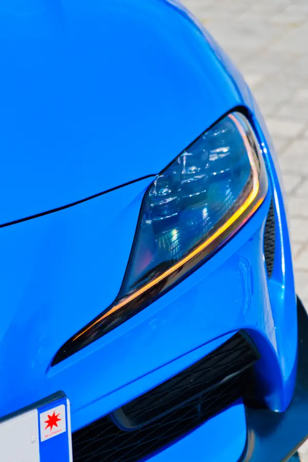 Gros plan sur le phare avant LED d'une Toyota Supra bleu électrique, montrant le design angulaire avec bande lumineuse orange intégrée.