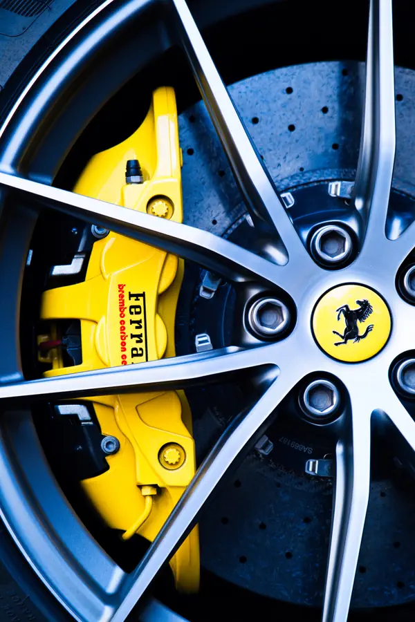 Gros plan sur une roue de Ferrari montrant un étrier de frein jaune vif avec l'inscription "Ferrari" en noir, derrière une jante en alliage gris à cinq branches.