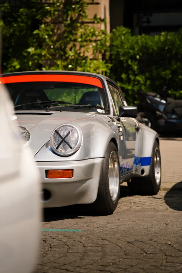 Porsche 911 classique modifiée dans un style course, de couleur blanche avec une bande orange sur le toit et une bande bleue sur le côté.
