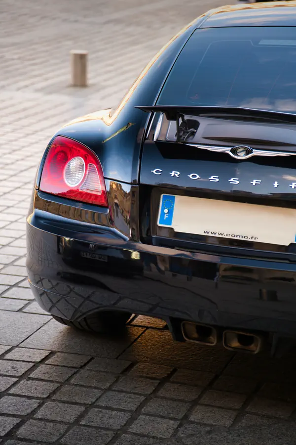 Détail de l'arrière d'une Chrysler Crossfire noire stationnée sur un sol pavé.