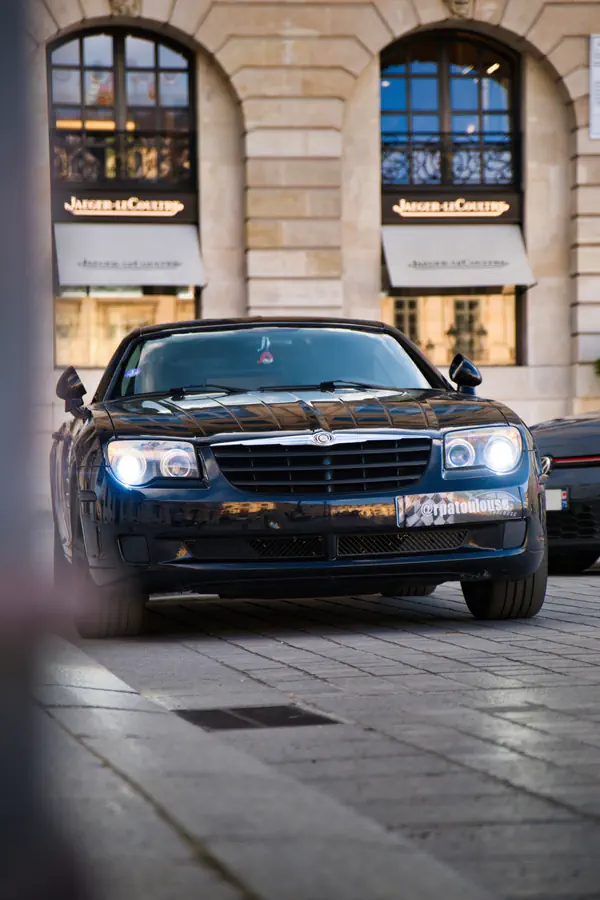 Chrysler Crossfire noire stationnée sur une place pavée devant la boutique Jaeger-LeCoultre.