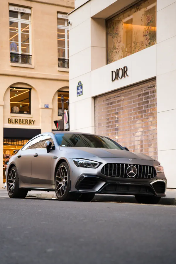 Mercedes-AMG GT gris mat stationnée dans une rue commerçante de luxe parisienne, devant les boutiques Dior et Burberry.