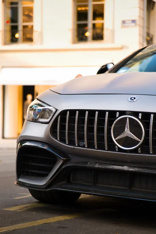 Gros plan sur l'avant d'une Mercedes-AMG GT gris mat montrant sa calandre Panamericana verticale caractéristique avec l'étoile Mercedes-Benz proéminente au centre, son phare LED et ses prises d'air agressives.