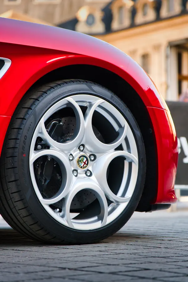 Gros plan sur la roue avant d'une Alfa Romeo 8C Spider rouge, montrant sa jante en alliage blanc à cinq cercles entrelacés avec l'écusson Alfa Romeo au centre.