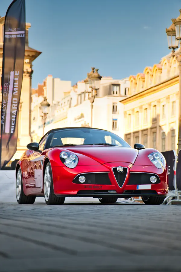 Alfa Romeo 8C Spider rouge photographiée de 3/4 avant gauche sur une place pavée.