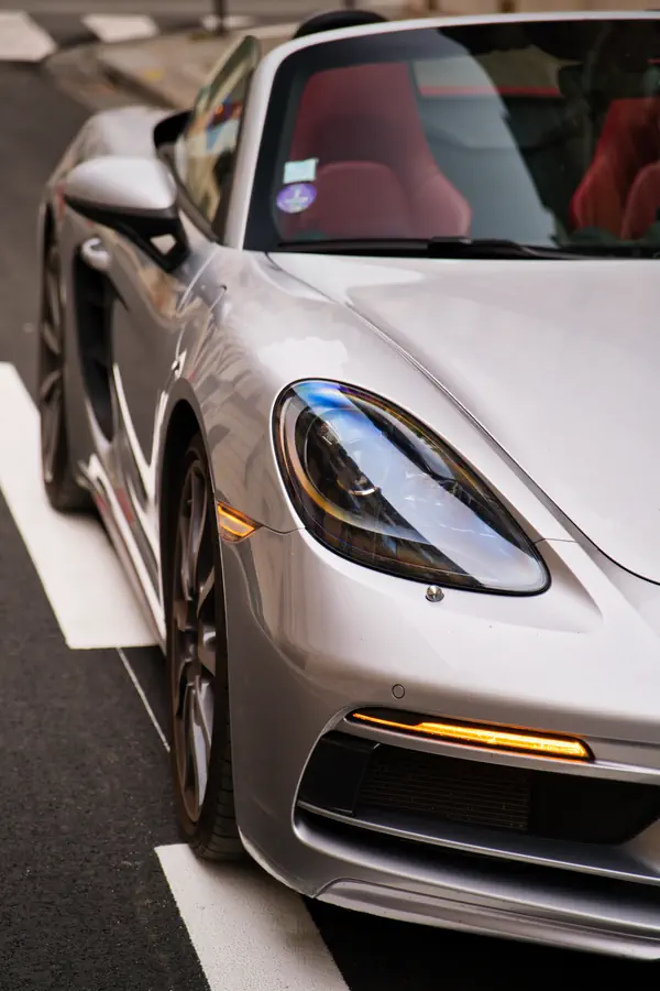 Gros plan sur l'avant d'une Porsche 718 Boxster gris argent, montrant son phare LED elliptique caractéristique et son clignotant LED orange intégré dans le pare-chocs.