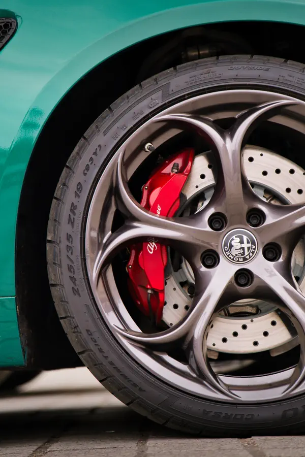Roue d'Alfa Romeo avec jante alliage gris anthracite à cinq branches, étriers de frein Brembo rouges et disques perforés, sur carrosserie vert menthe.