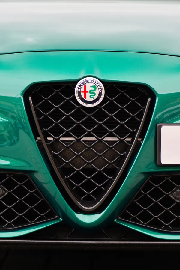 Gros plan sur la calandre triangulaire emblématique d'une Alfa Romeo de couleur vert émeraude métallisé.