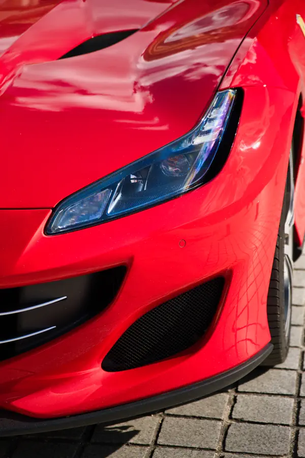 Phare avant LED d'une Ferrari Portofino rouge avec optiques bleutées et prises d'air latérales en nid d'abeille noir.
