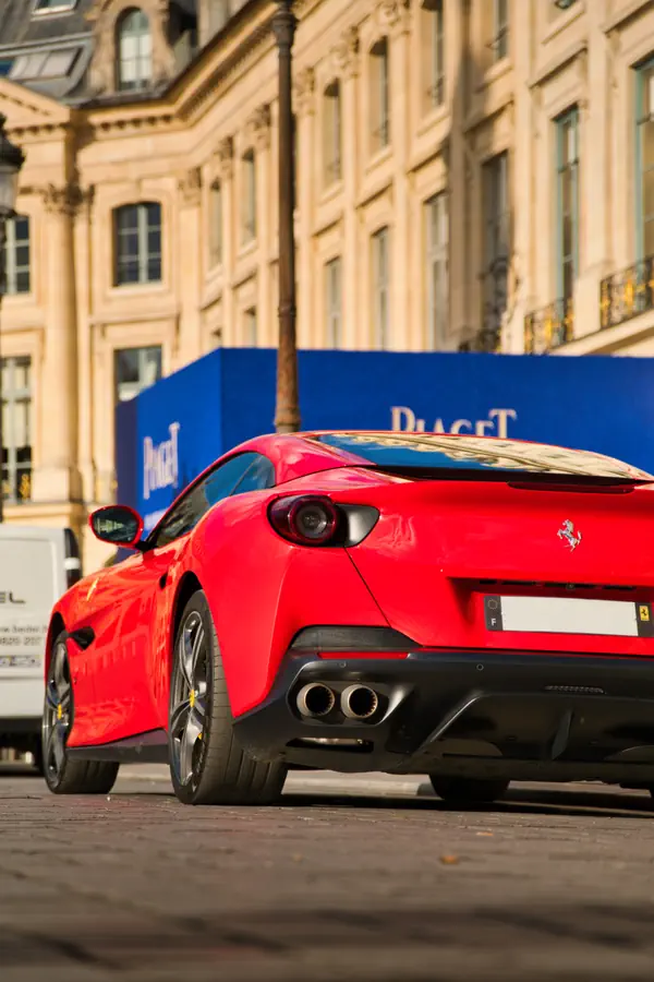 Ferrari Portofino rouge vue de trois-quarts arrière avec double échappement circulaire, stationnée devant architecture haussmannienne en pierre.