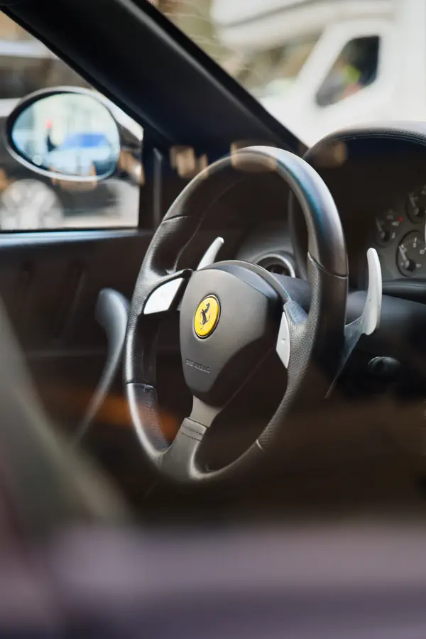 Intérieur de Ferrari avec volant noir à logo cheval cabré jaune, palettes de changement de vitesses argentées et tableau de bord sombre.