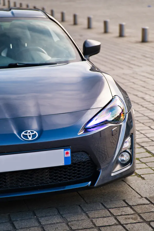 Toyota GT86 gris foncé, vue de trois quarts avant droit, mettant en évidence le phare et le logo Toyota, garée sur un sol pavé.