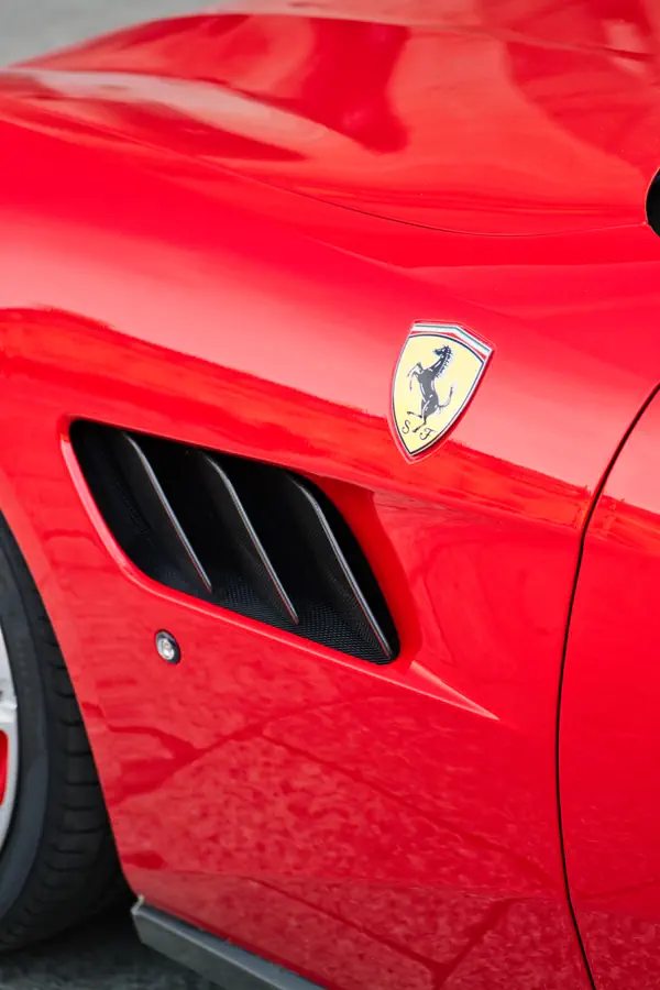 Gros plan sur l'aile d'une Ferrari rouge vif, mettant en évidence la prise d'air latérale noire et l'écusson du cheval cabré.