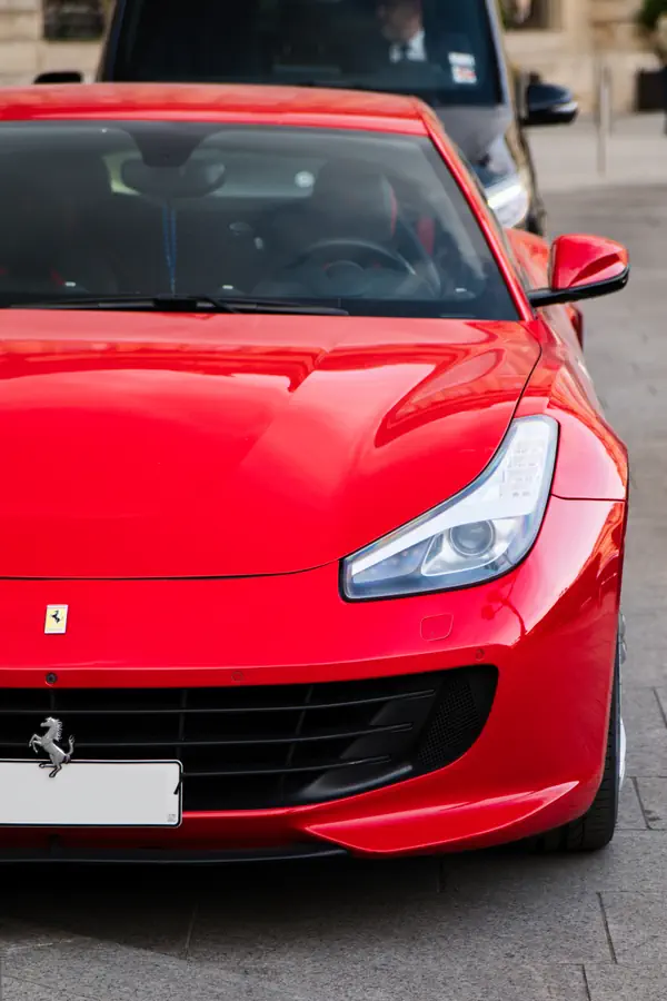Vue avant d'une Ferrari rouge vif, mettant en évidence son phare profilé et l'emblème du cheval cabré sur la calandre.
