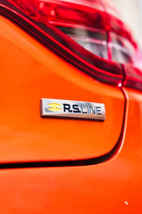 Gros plan sur le badge "R.S. line" sur la carrosserie orange d'une voiture, situé juste en dessous du feu arrière.