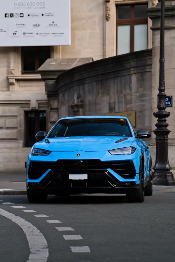 Lamborghini Urus bleu vif photographié de face, garé dans une rue parisienne avec une architecture en pierre en arrière-plan.