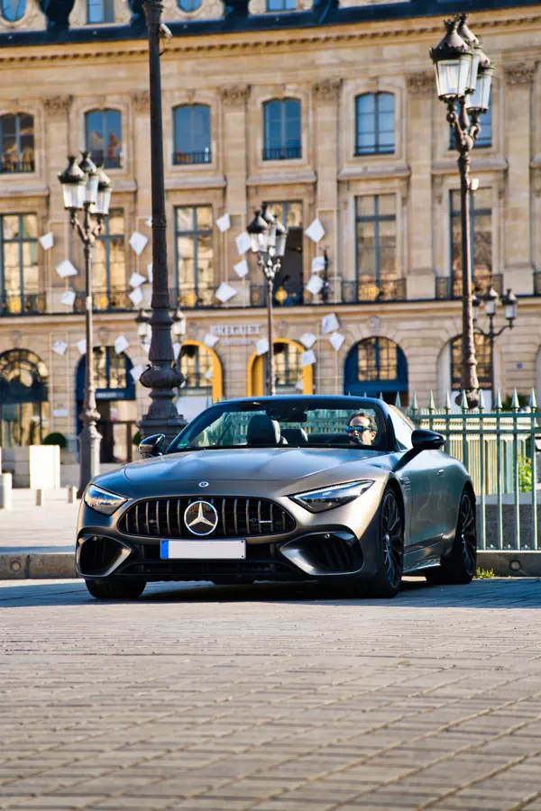 Mercedes-AMG SL décapotable de couleur gris, garée sur les pavés de la Place Vendôme à Paris, avec les façades et lampadaires classiques du lieu en arrière-plan.