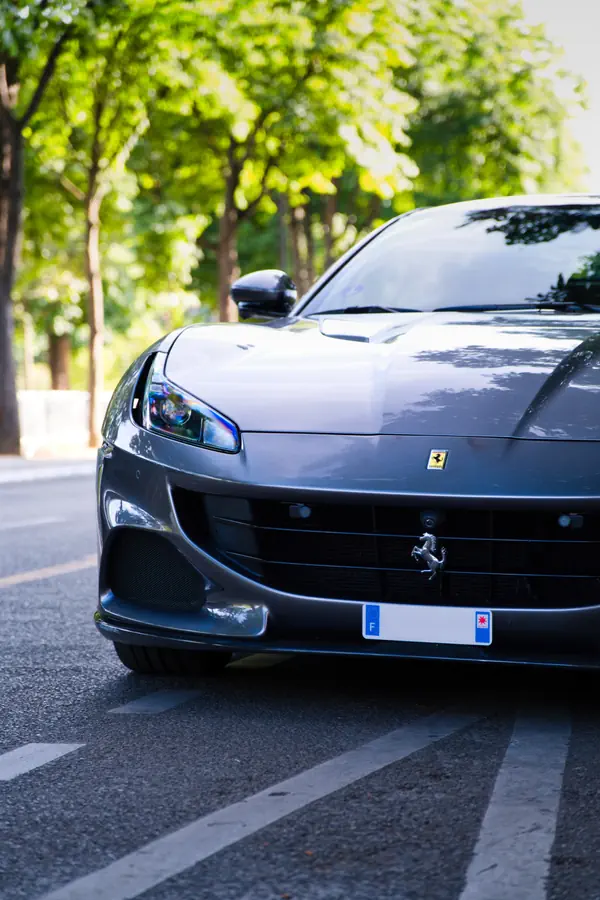 Ferrari Portofino gris foncé, vue de trois-quarts avant prise à ras du sol, garée sur une avenue bordée d'arbres.