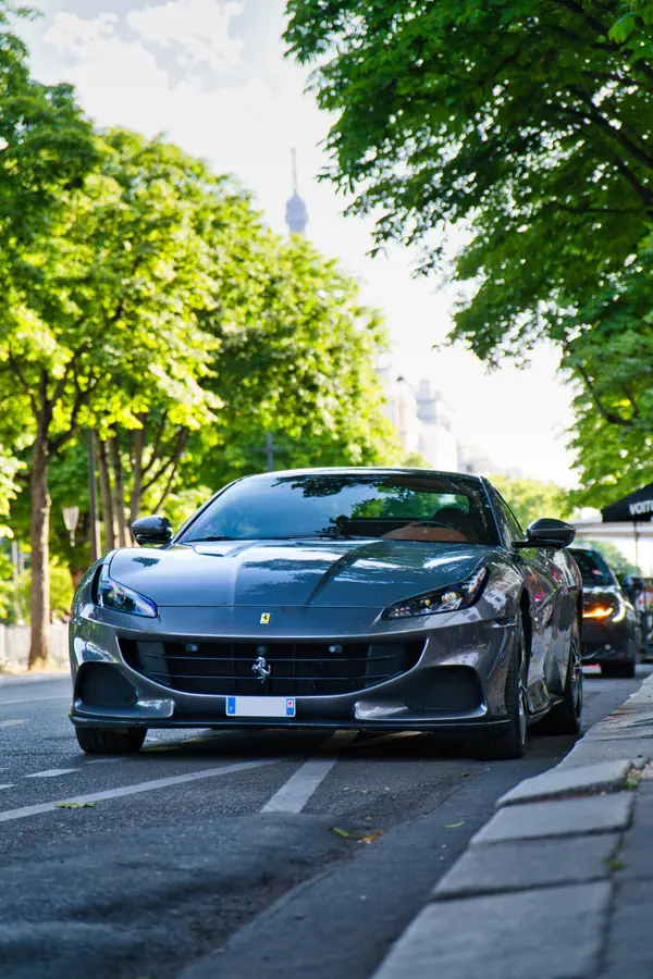 Ferrari Portofino M de couleur gris foncé, garée sur une avenue parisienne ensoleillée et bordée d'arbres, avec la Tour Eiffel visible au loin.