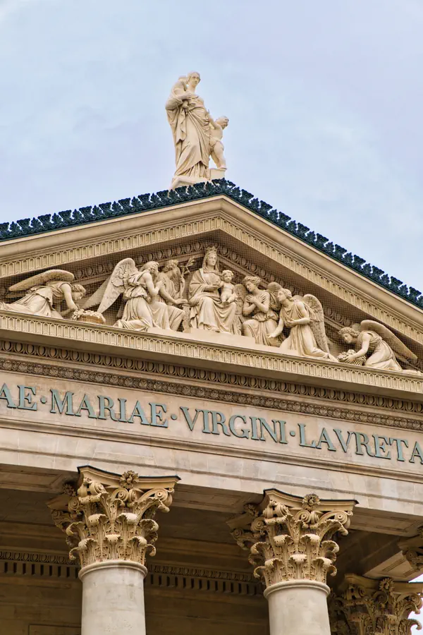 Détail de la façade de l'église Notre-Dame-de-Lorette à Paris, montrant le fronton triangulaire sculpté, l'inscription latine "BEATAE·MARIAE·VIRGINI·LAVRETANAE", et les chapiteaux de style corinthien des colonnes.
