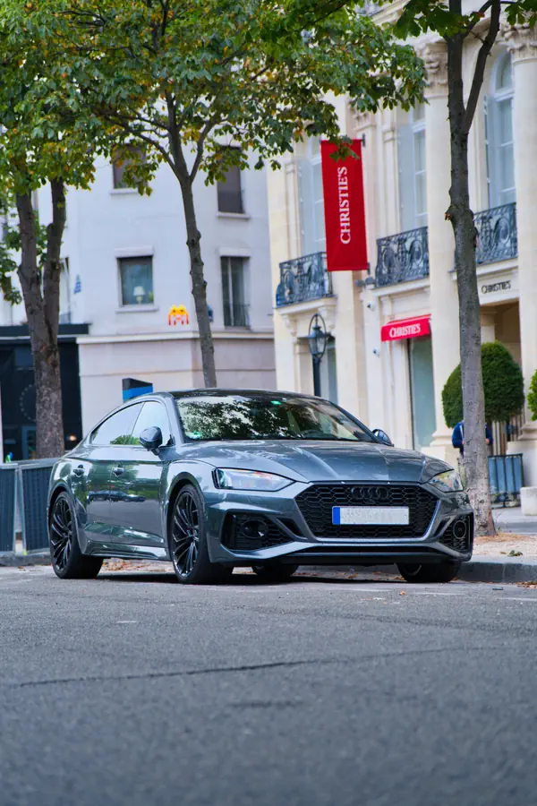 Audi RS 5 Sportback de couleur gris nardo garée dans une rue parisienne, avec en arrière-plan l'immeuble de la maison de vente aux enchères Christie's.