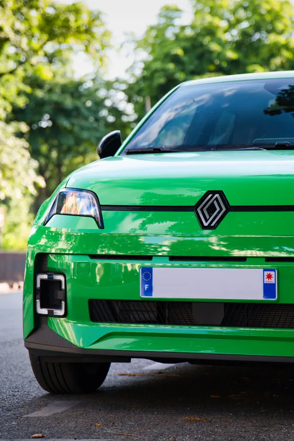 Gros plan sur l'avant de la nouvelle Renault 5 E-Tech électrique de couleur vert vif, mettant en évidence le phare, le logo Renault et les feux de jour rectangulaires dans le pare-chocs.