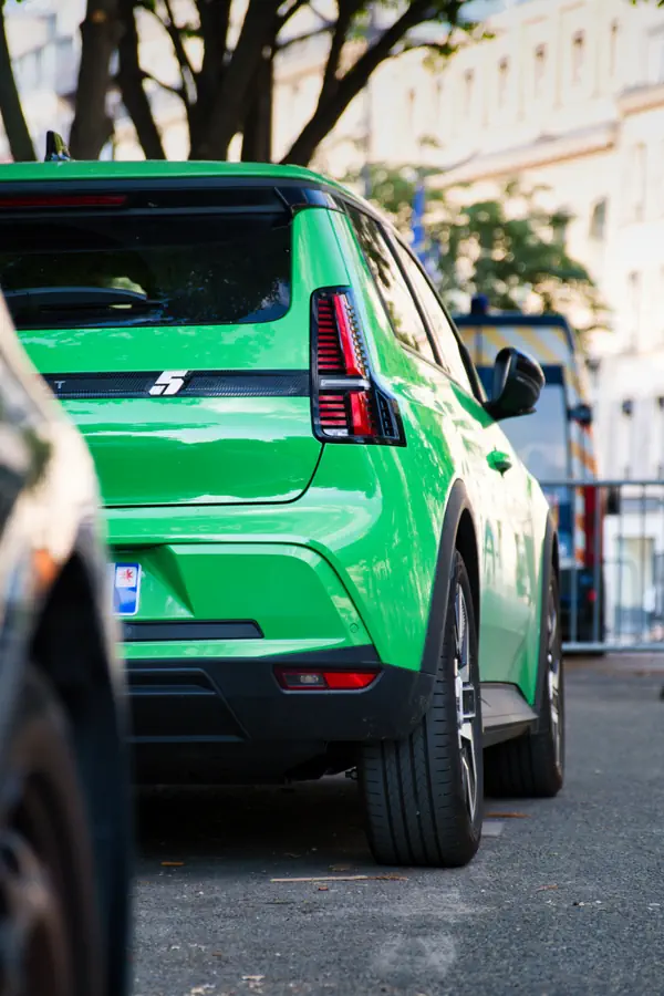 Vue de trois-quarts arrière de la nouvelle Renault 5 E-Tech électrique de couleur verte, mettant en évidence le design de son feu arrière vertical et le logo "5" sur le hayon.