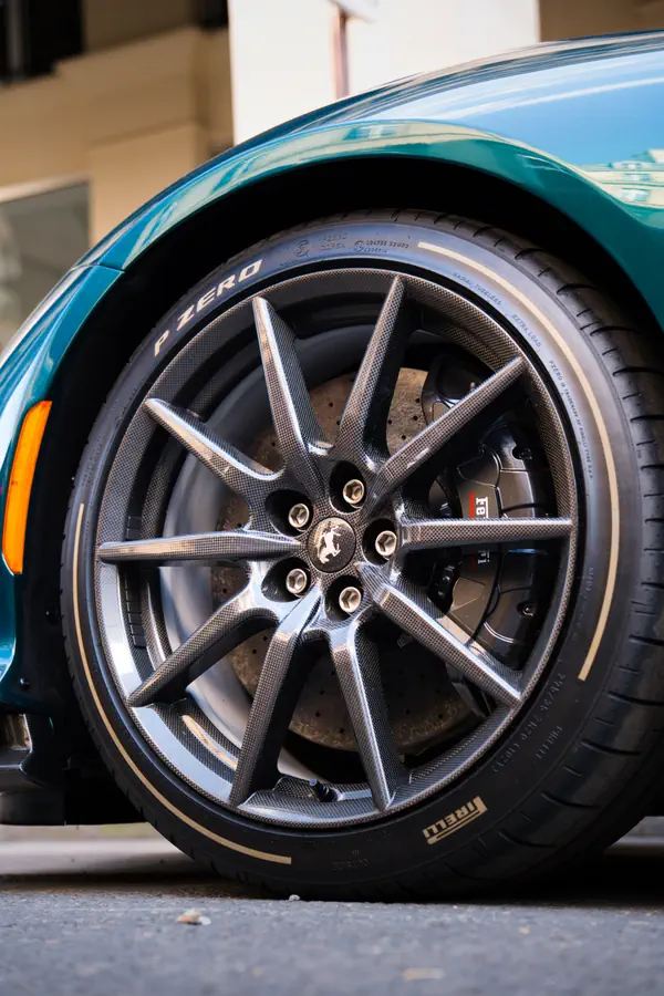 Gros plan sur la roue d'une Ferrari 812 Competizione, montrant la jante en fibre de carbone, l'étrier de frein noir siglé "Ferrari", et le pneu Pirelli P Zero.