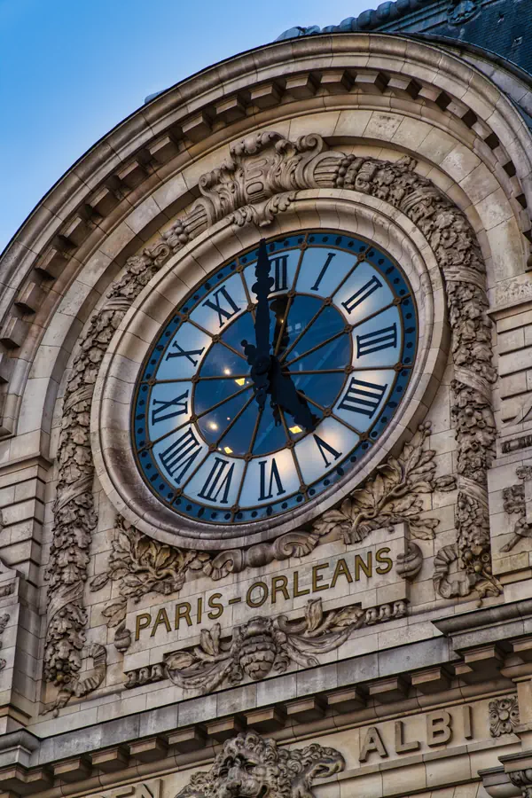 Grande horloge monumentale de la gare Paris-Orléans avec son cadran à chiffres romains sur fond bleu, encadrée de décorations sculptées en pierre et surmontant l'inscription "PARIS-ORLEANS".