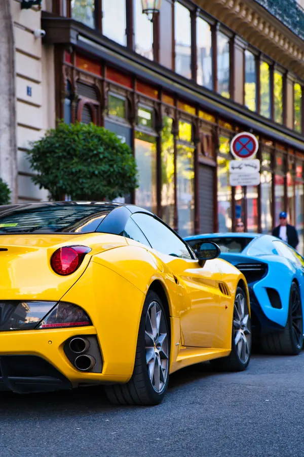 Ferrari California T de couleur jaune vif, vue de trois-quarts arrière, garée dans une rue parisienne juste devant une McLaren de couleur bleu clair.
