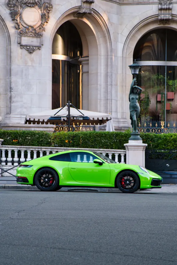 Vue de profil d'une Porsche 911 moderne de couleur vert vif, garée devant la façade ornée de l'Opéra Garnier à Paris.