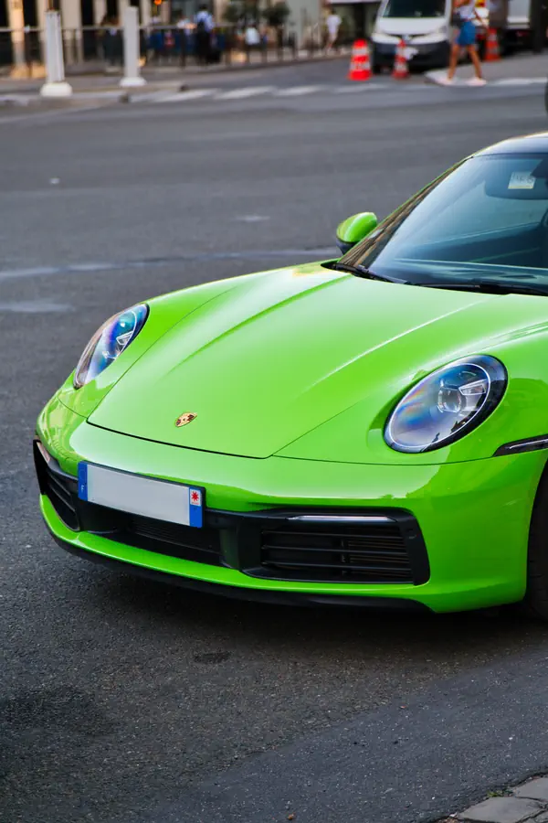 Gros plan sur l'avant d'une Porsche 911 moderne de couleur vert vif, mettant en évidence son phare rond emblématique et l'écusson Porsche sur le capot.