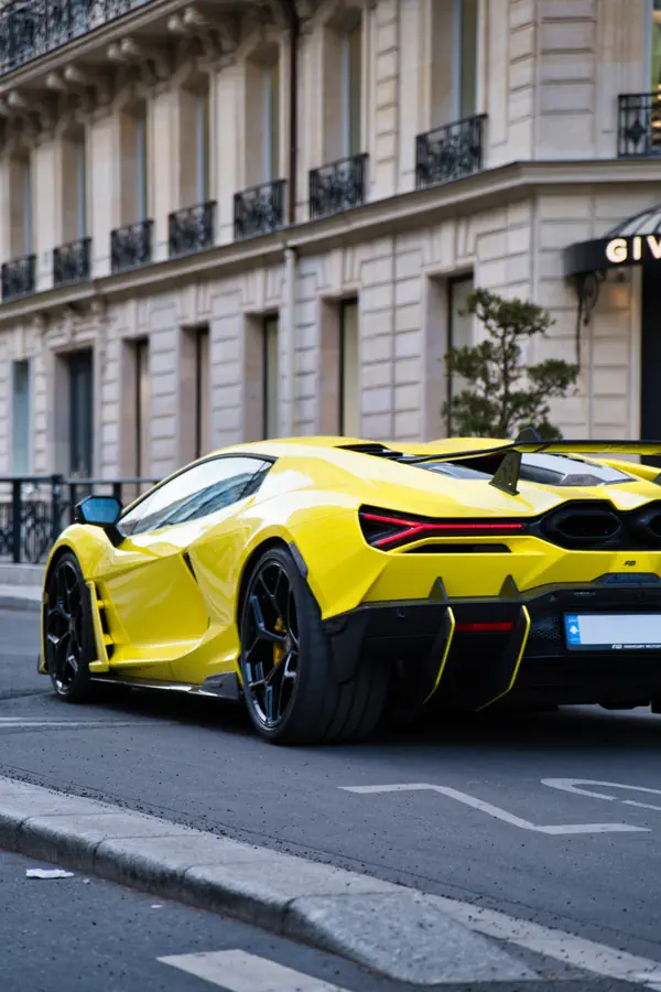 Vue de trois-quarts arrière d'une Lamborghini Revuelto de couleur jaune vif, mettant en évidence son design futuriste avec ses feux arrière hexagonaux et son aileron en carbone, garée dans une rue de luxe à Paris.