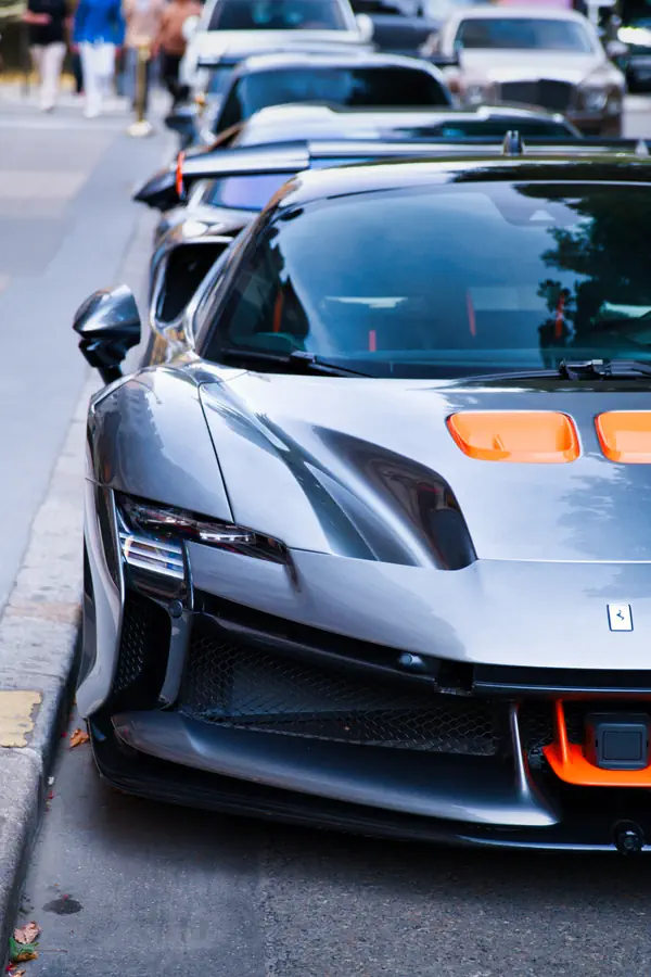 Gros plan sur l'avant de la Ferrari SF90 XX Stradale, un modèle unique de couleur grise, mettant en évidence son design futuriste, ses phares très fins et ses aérations de capot orange vif.