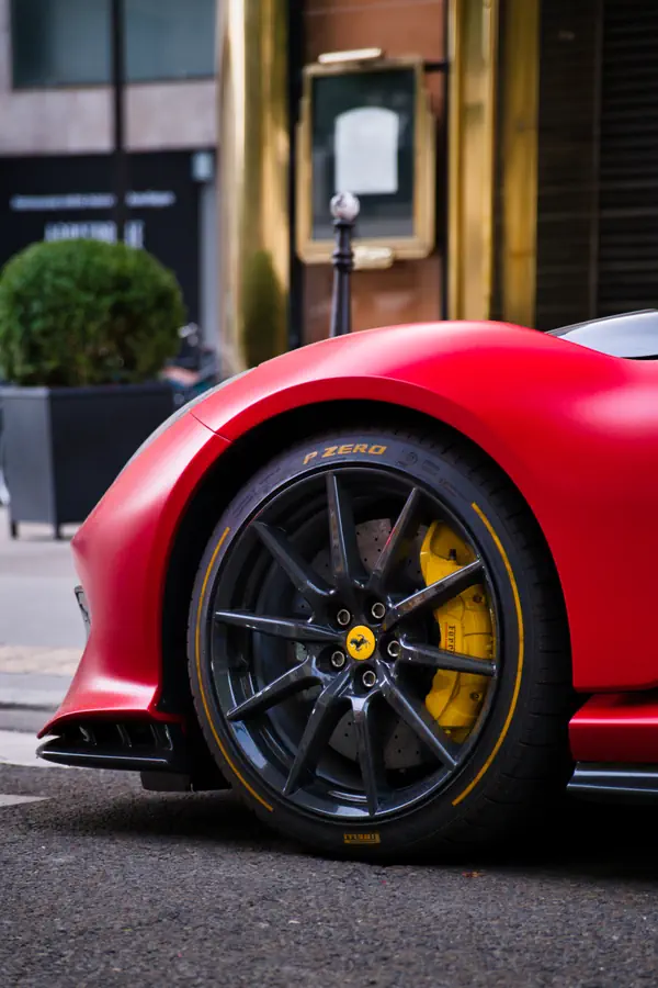 Gros plan sur la roue avant d'une Ferrari avec une peinture rouge mat. La jante est en fibre de carbone, l'étrier de frein est jaune vif, et le pneu Pirelli P Zero est souligné d'un liseré jaune assorti.