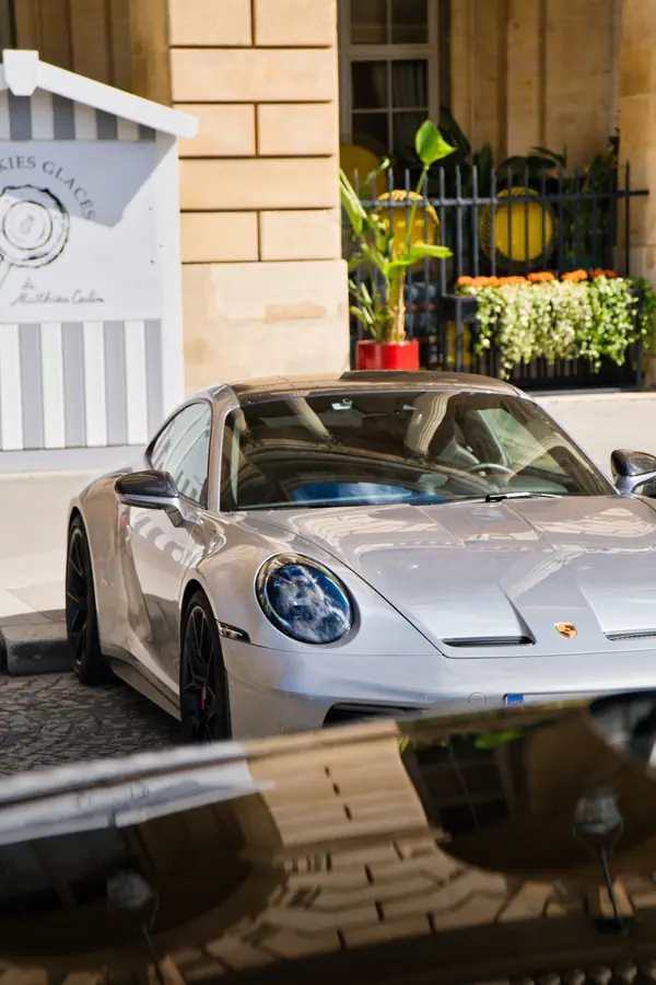 Porsche 911 grise métallisée stationnée devant un bâtiment classique en pierre de taille