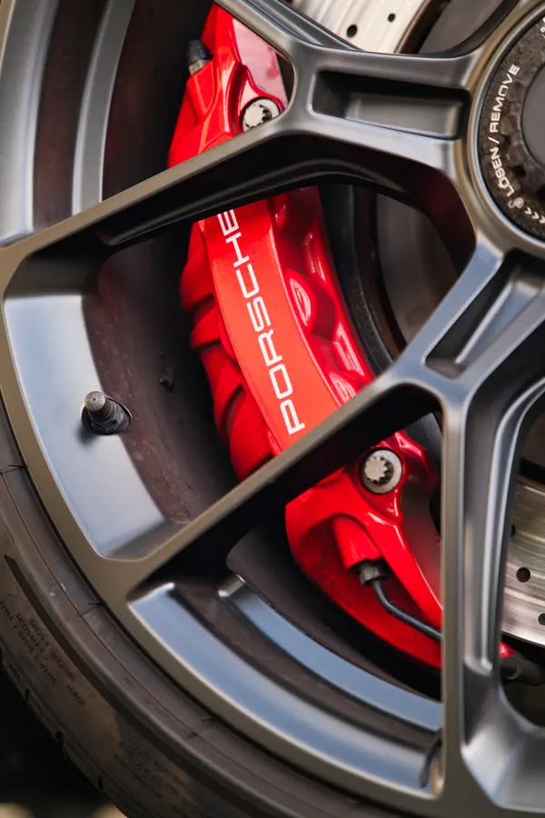 Gros plan sur une jante en alliage gris foncé d'une Porsche, révélant un étrier de frein rouge vif avec l'inscription "PORSCHE" en blanc et un disque de frein percé.